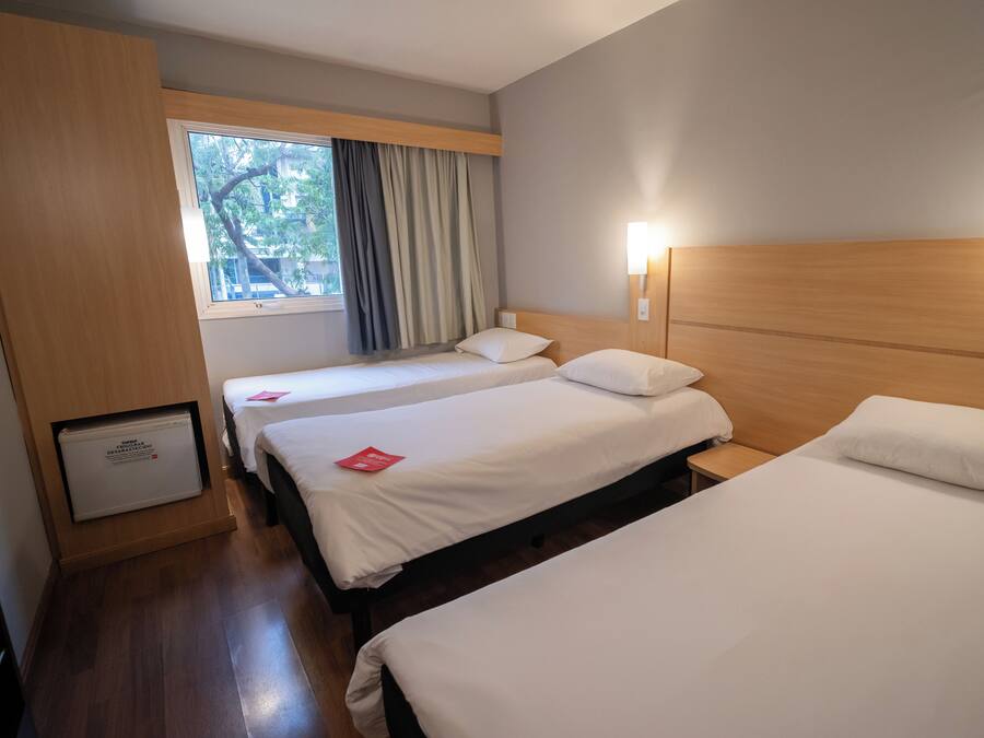 Ein Hotelzimmer mit zwei Betten, einem Fenster mit Vorhängen, einer Wandlampe und einem kleinen Schrank.