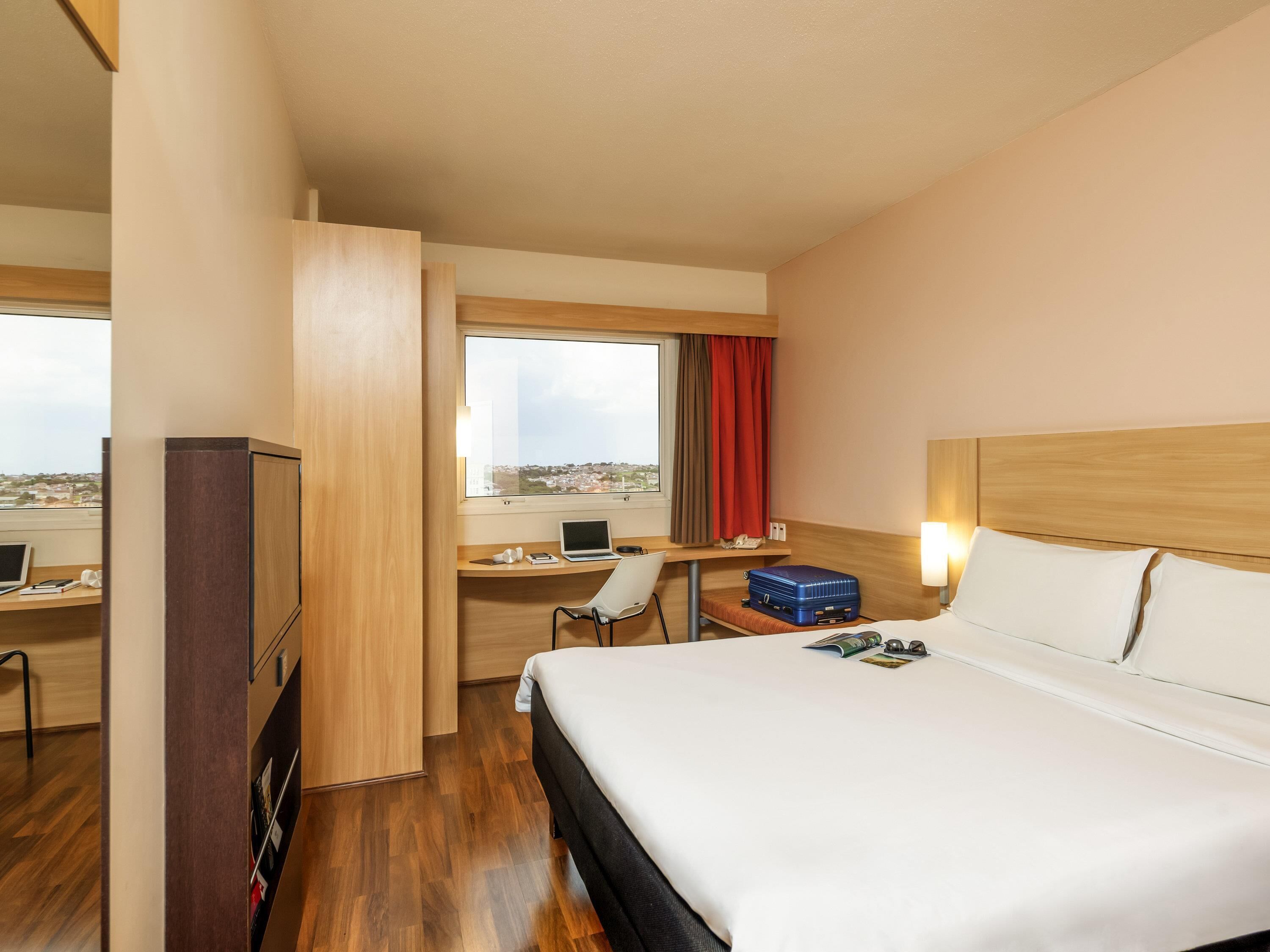 Habitación de hotel con cama, escritorio, silla y vista a la ciudad.