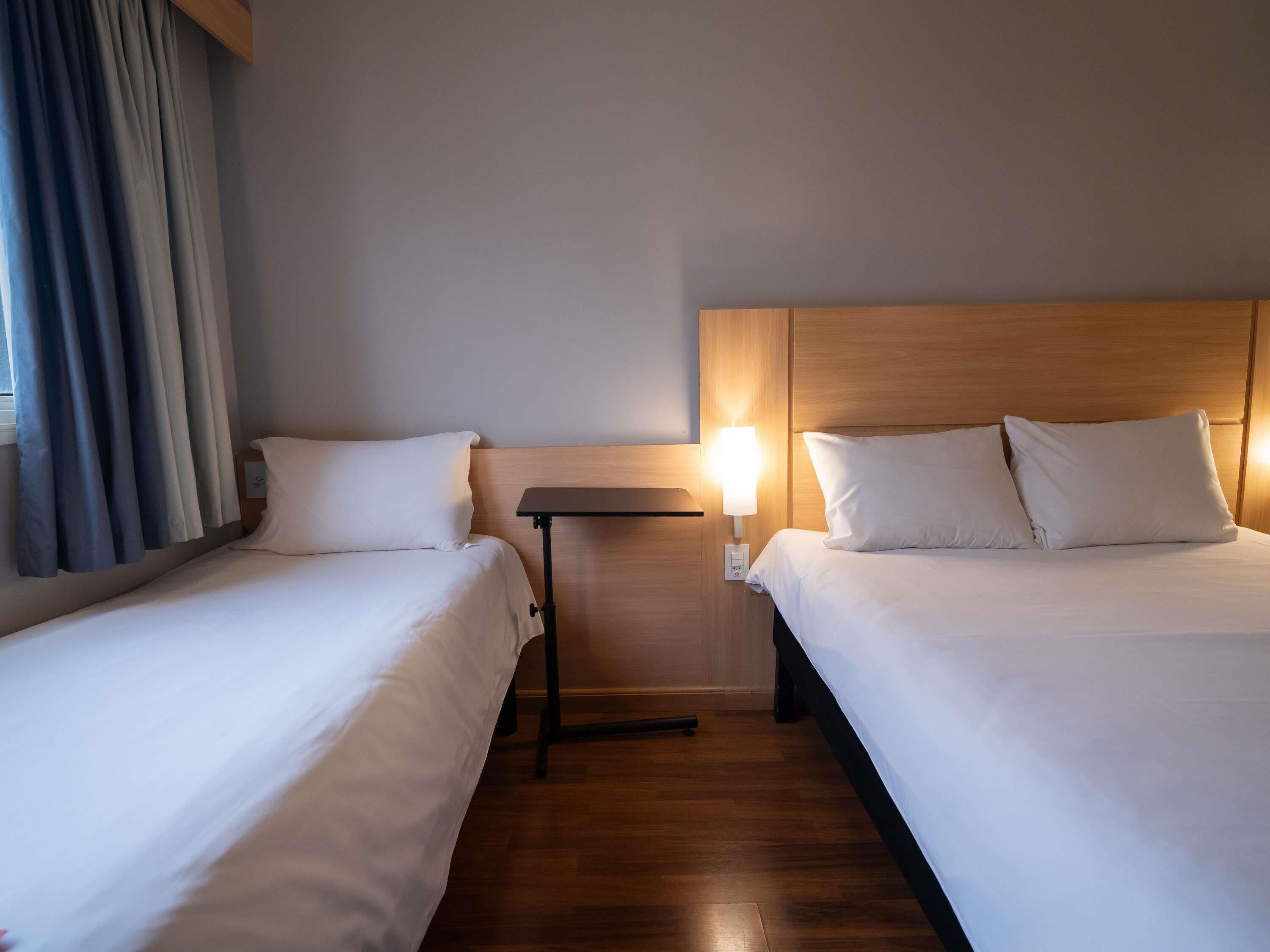 A hotel room with two beds, a nightstand, and a wall-mounted lamp.