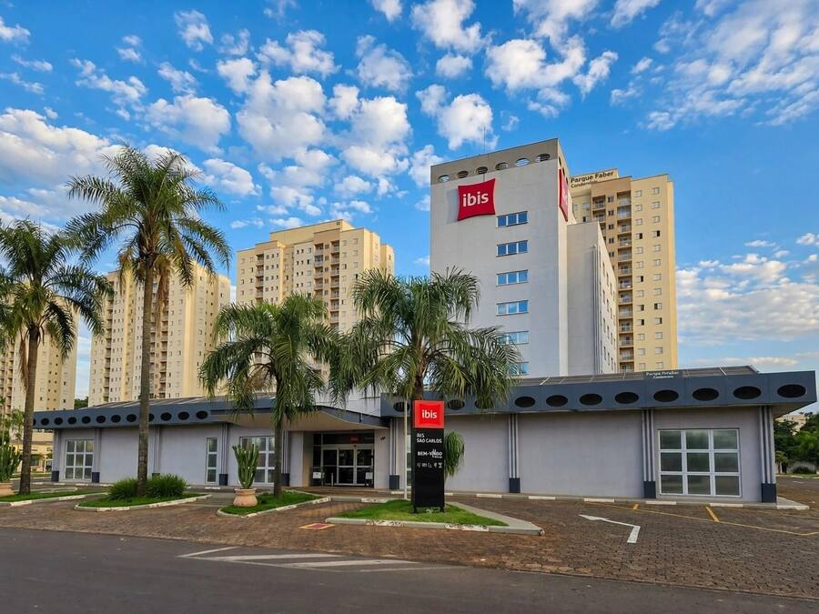 A modern hotel with a prominent ibis logo, surrounded by palm trees and adjacent high-rise buildings.