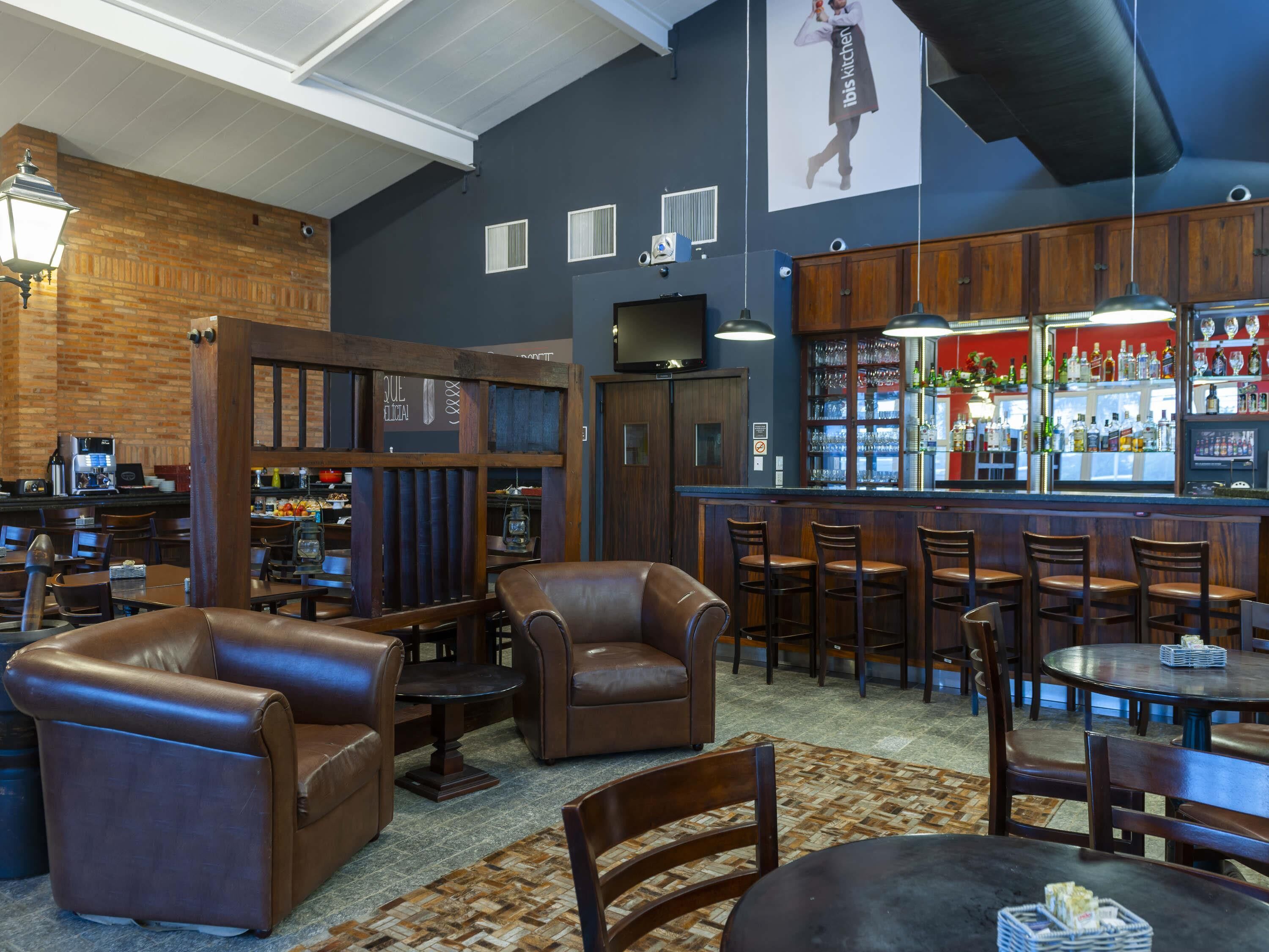 A bar area with leather seating, a bar counter with a red backdrop, and a visible menu board.