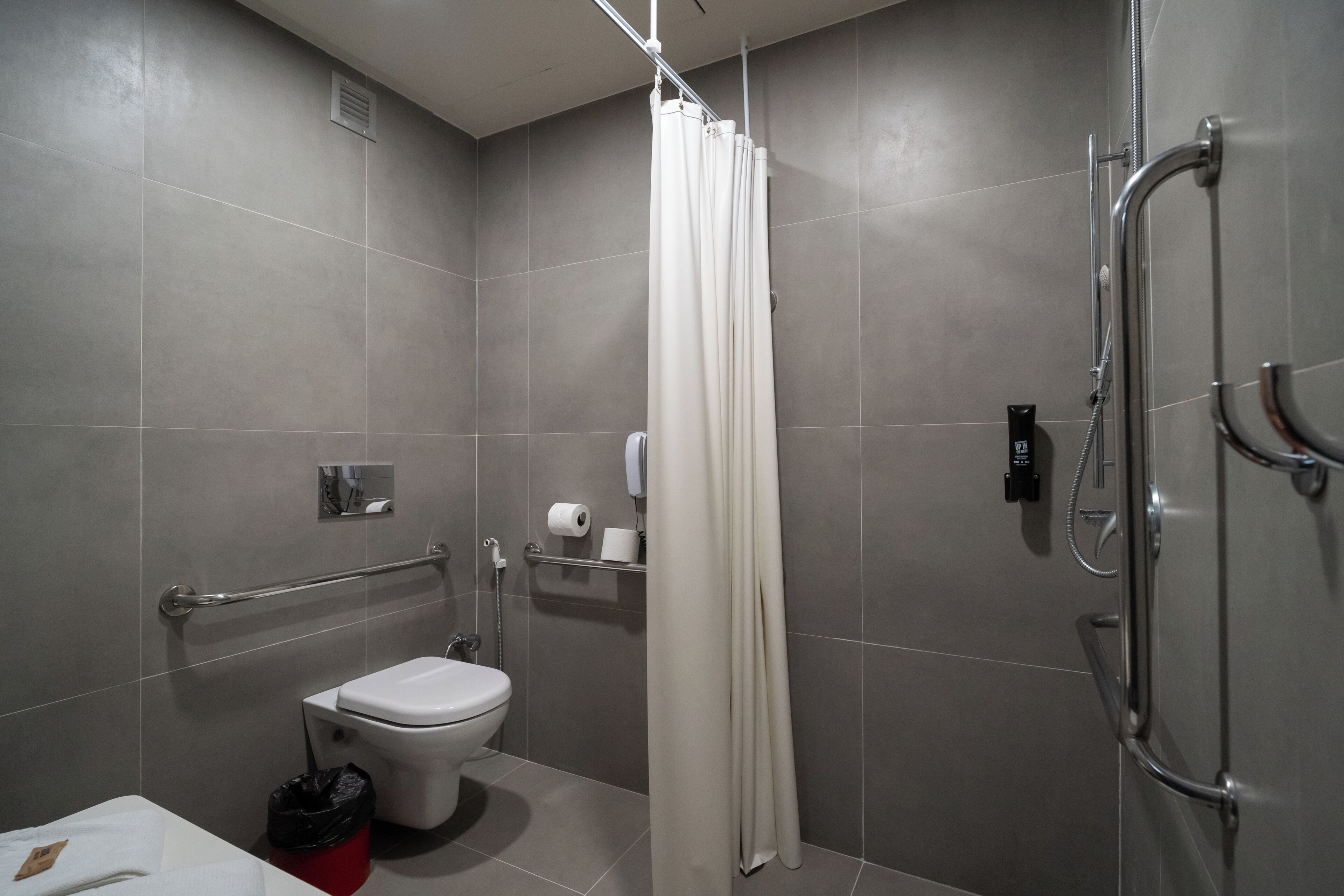 Une salle de bain moderne équipée de toilettes, d’une douche, de barres d’appui et d’un porte-serviettes.