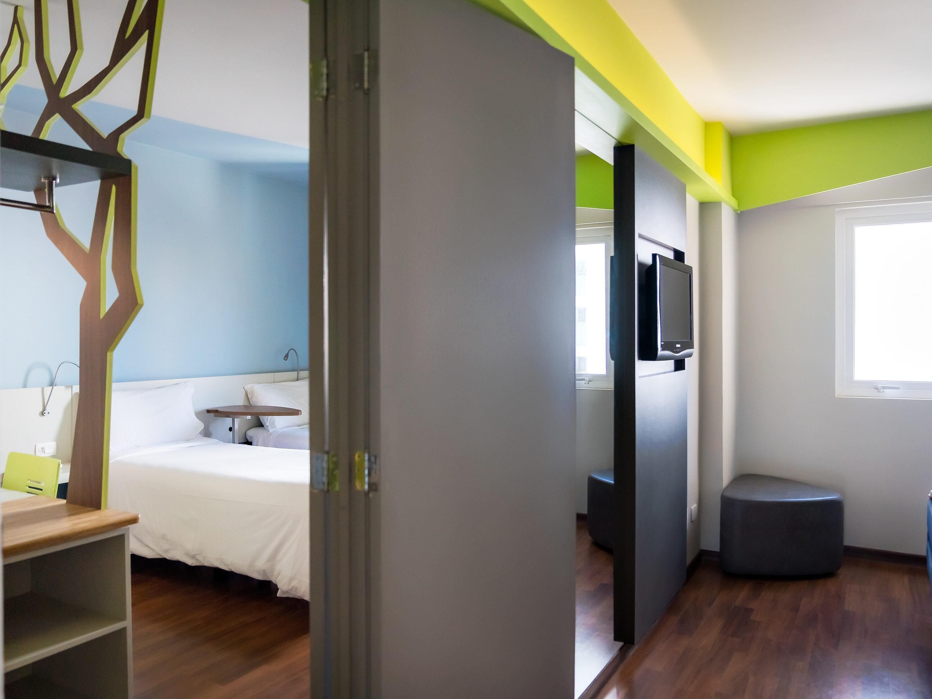 A hotel room with a bed, a desk, a chair, a television, and a window.