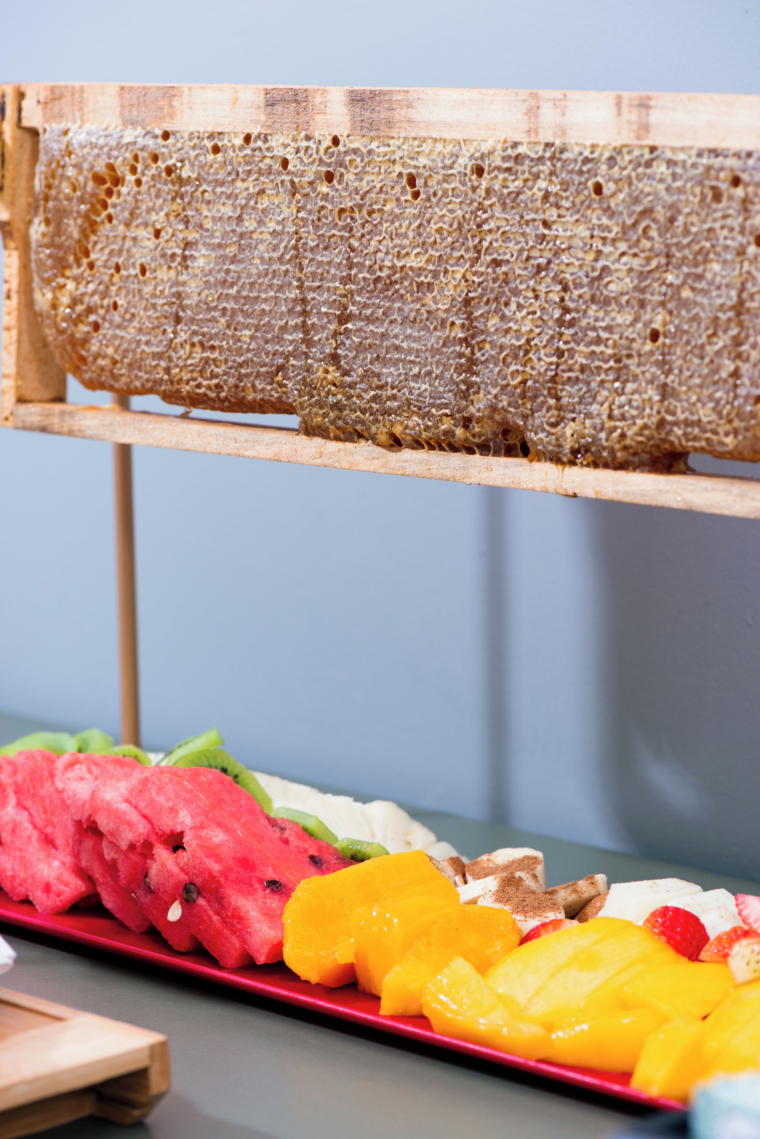 Una estructura de panal sobre un soporte de madera, una bandeja roja con diversas frutas y una mesa de madera.