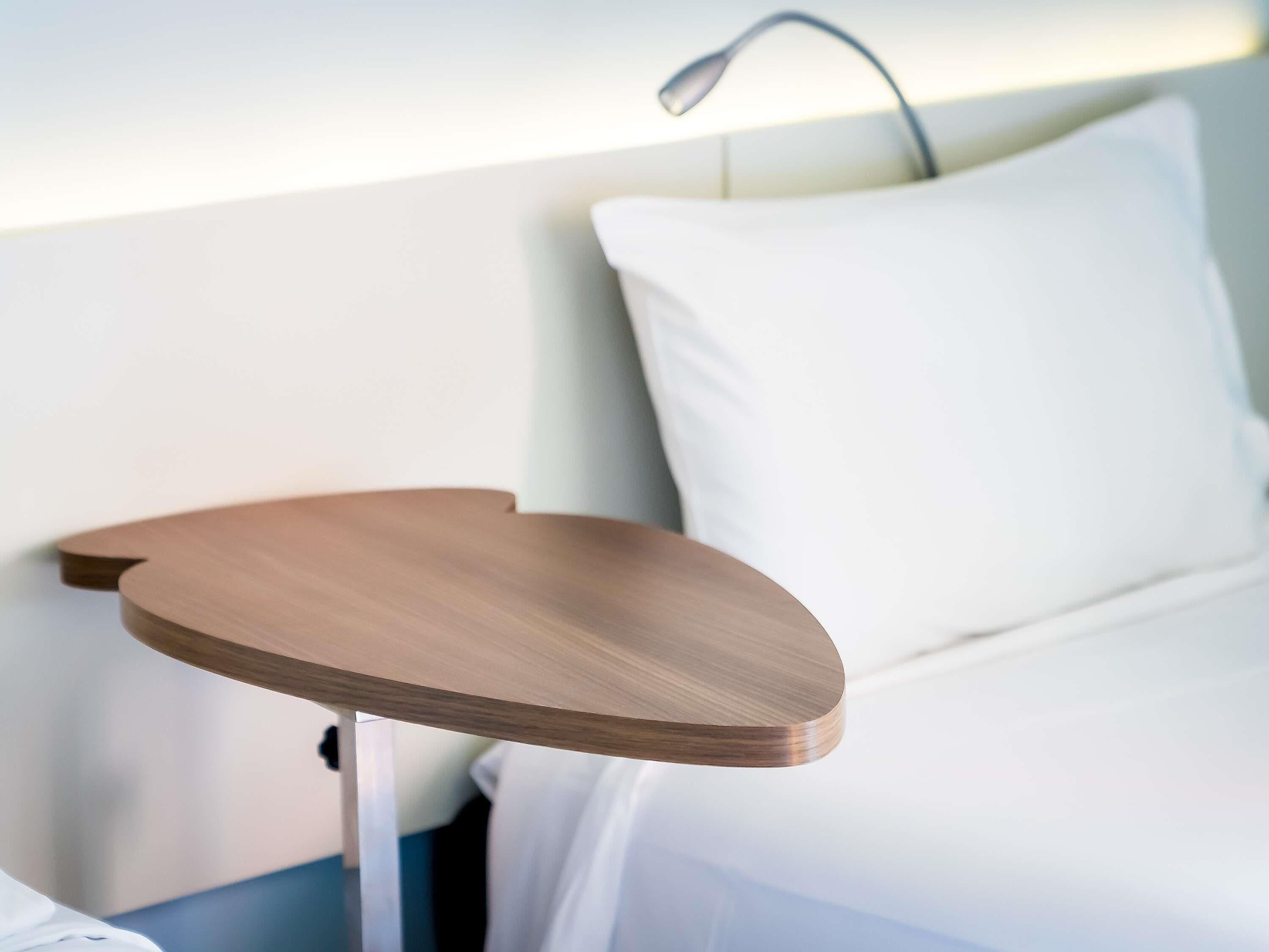 A bed with white pillows and a wooden bedside table.