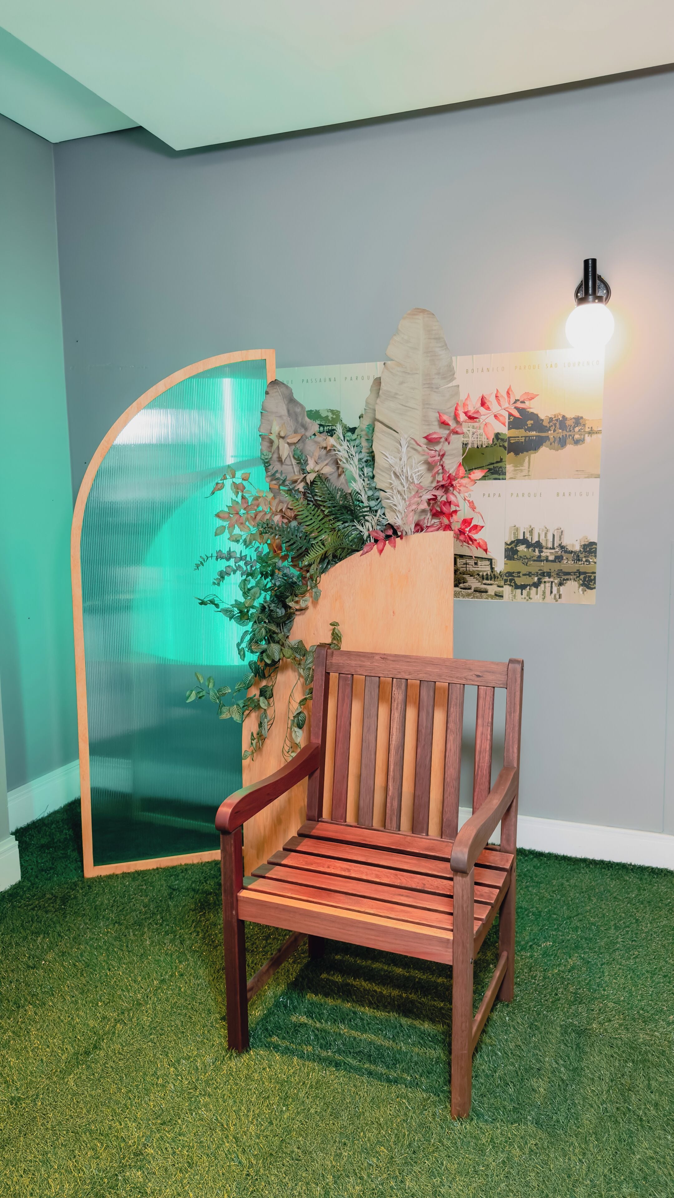 Un banco de madera en una habitación con césped artificial, un aplique de pared y un cartel con un paisaje urbano.