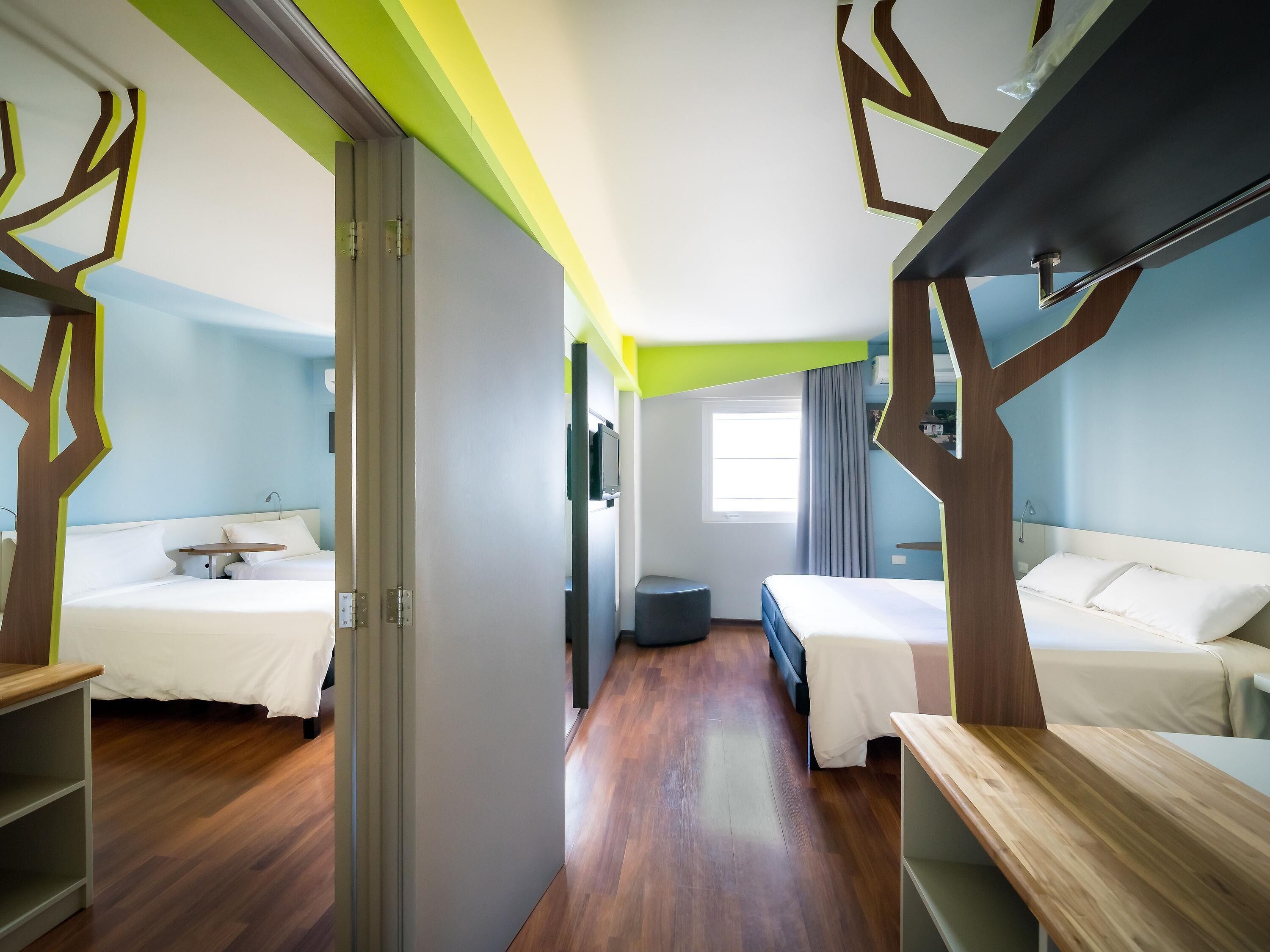 Quarto de hotel com duas camas, uma escrivaninha e um pequeno espaço para sentar.