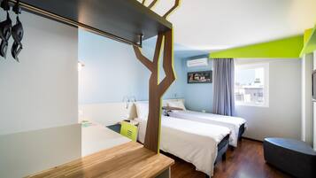 Habitación de hotel con dos camas, un escritorio, una silla, un televisor y ventana con vista a la ciudad.