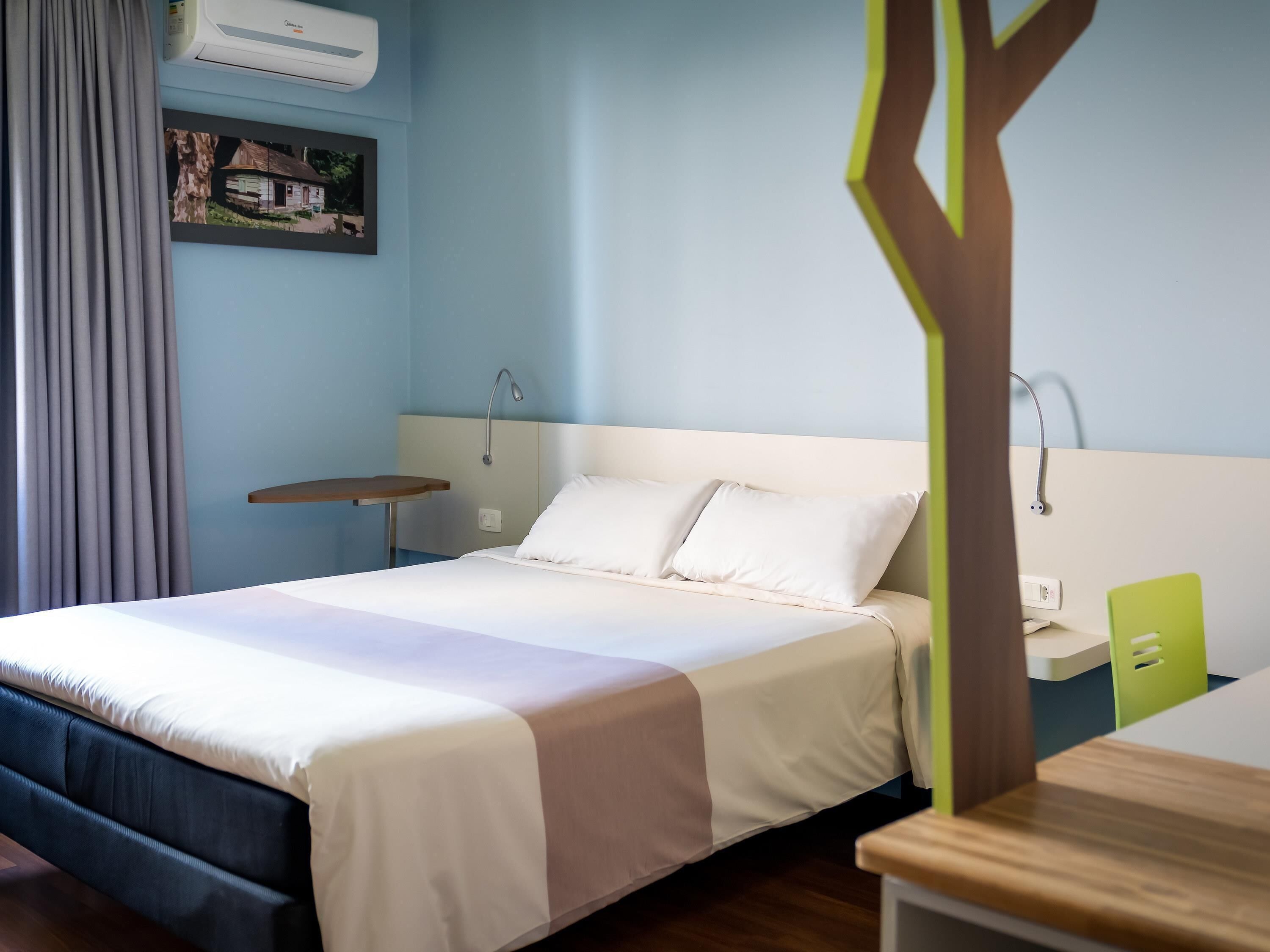 A neatly arranged hotel room with a bed, bedside table, and a small table with a lamp.
