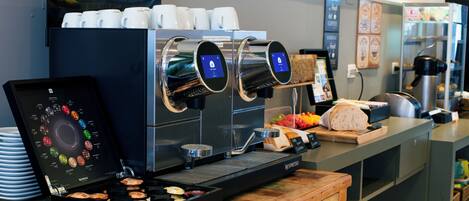 Una estación de café con una máquina de espresso, una exhibición de tazas de café y una variedad de pasteles.