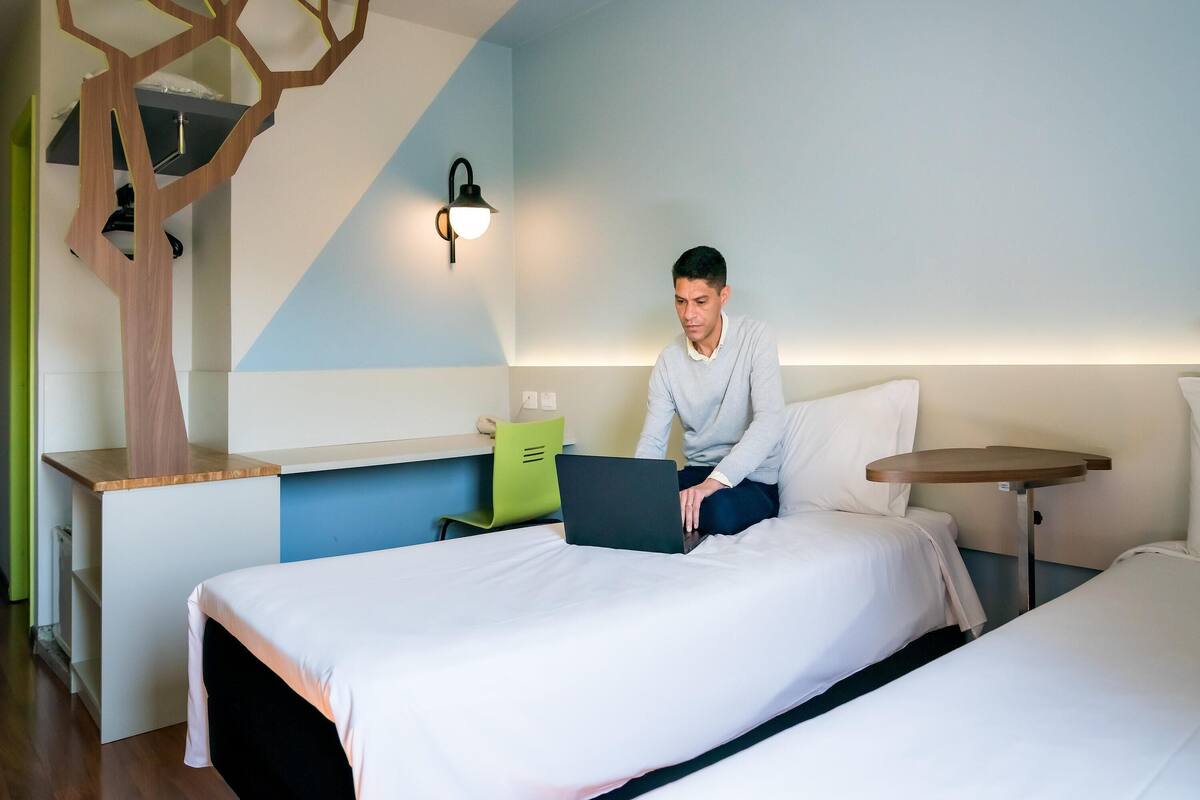Een hotelkamer met een bed, een bureau met een laptop, een klein tafeltje en een wandlamp.