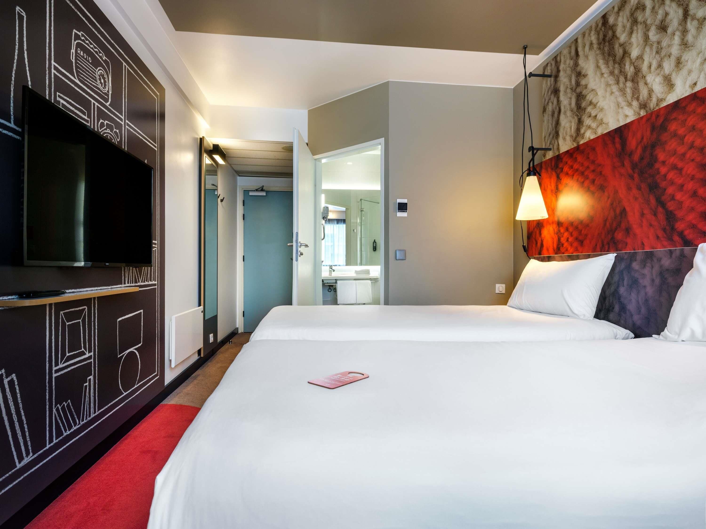 Une chambre d’hôtel avec un grand lit, un téléviseur à écran plat, un miroir et une moquette rouge.