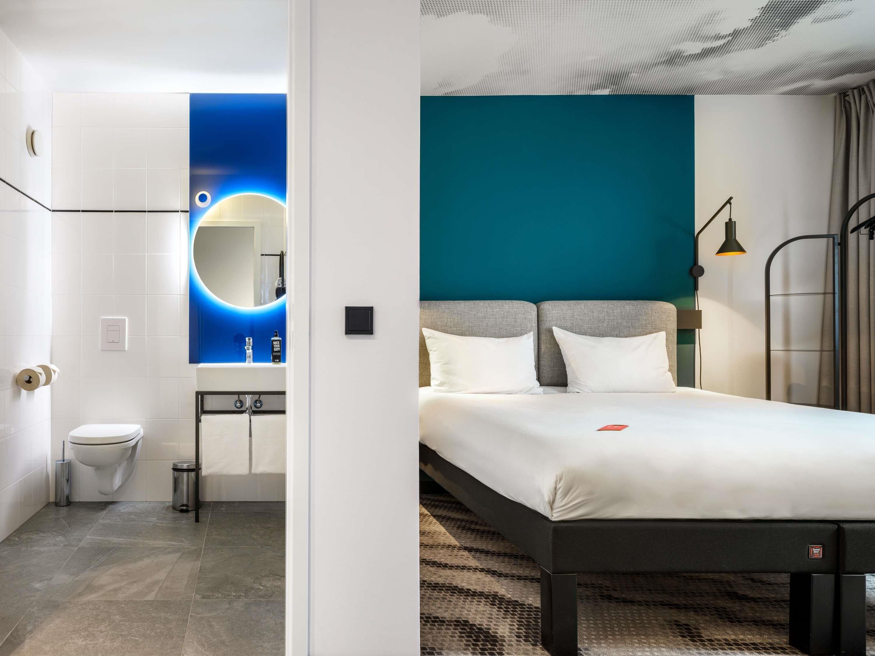 Une chambre d’hôtel moderne, dotée d’un lit, d’une salle de bain et offrant une vue sur le paysage urbain.