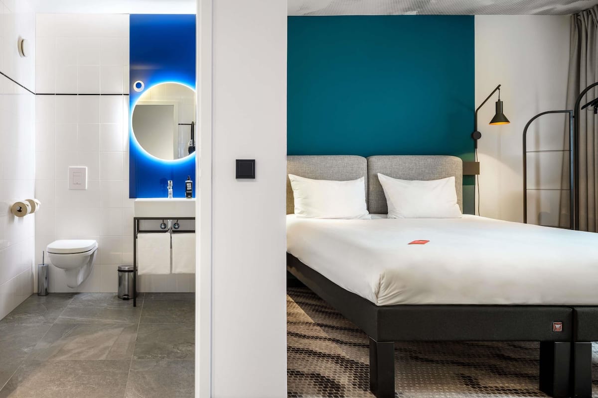 Une chambre dâhĂŽtel moderne, dotĂ©e dâun lit, dâune salle de bain et offrant une vue sur le paysage urbain.