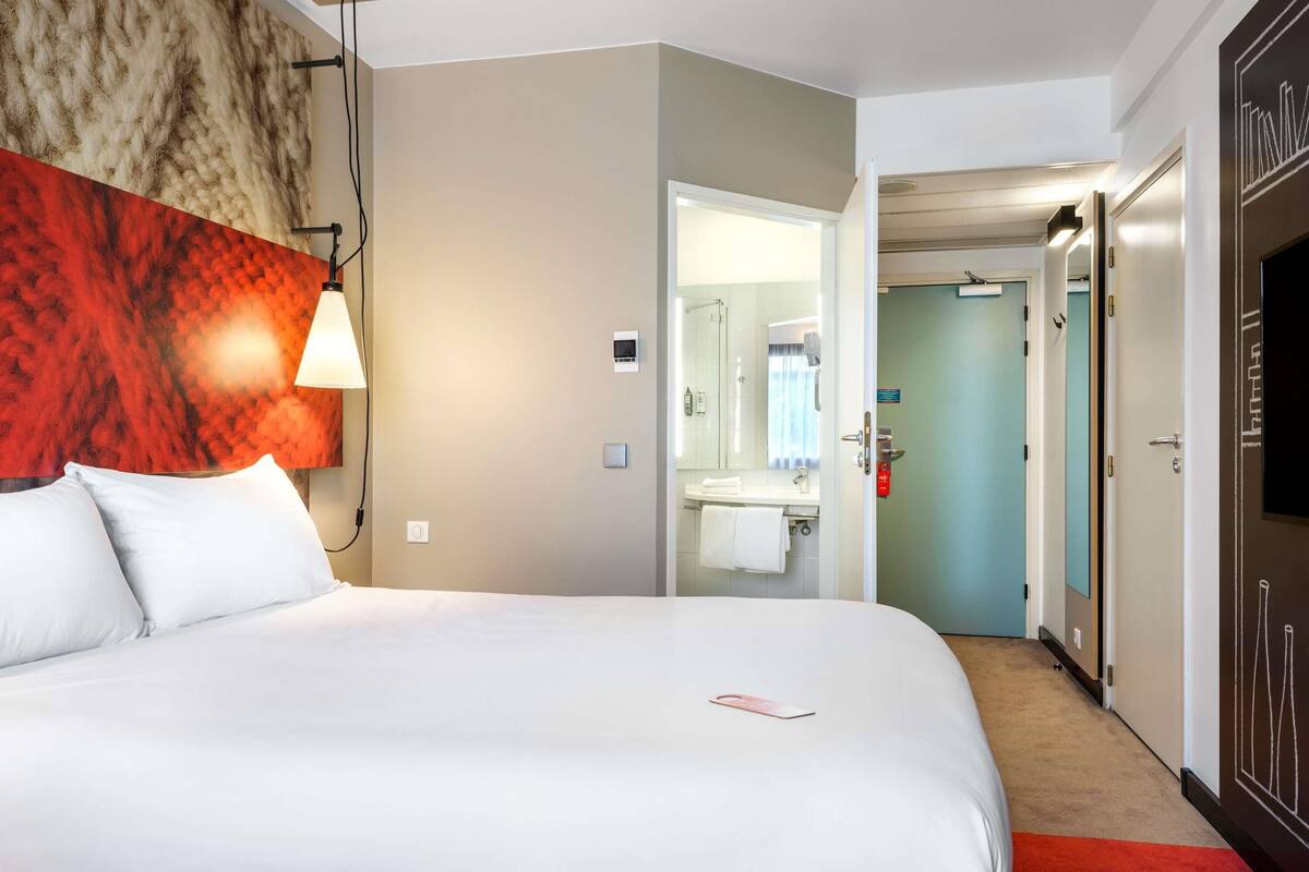 A hotel room with a bed, a bathroom with a mirror, and a TV.