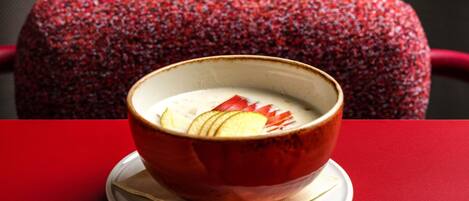 A bowl of soup with apple slices on a white plate, placed on a red table with a red chair in the background.
