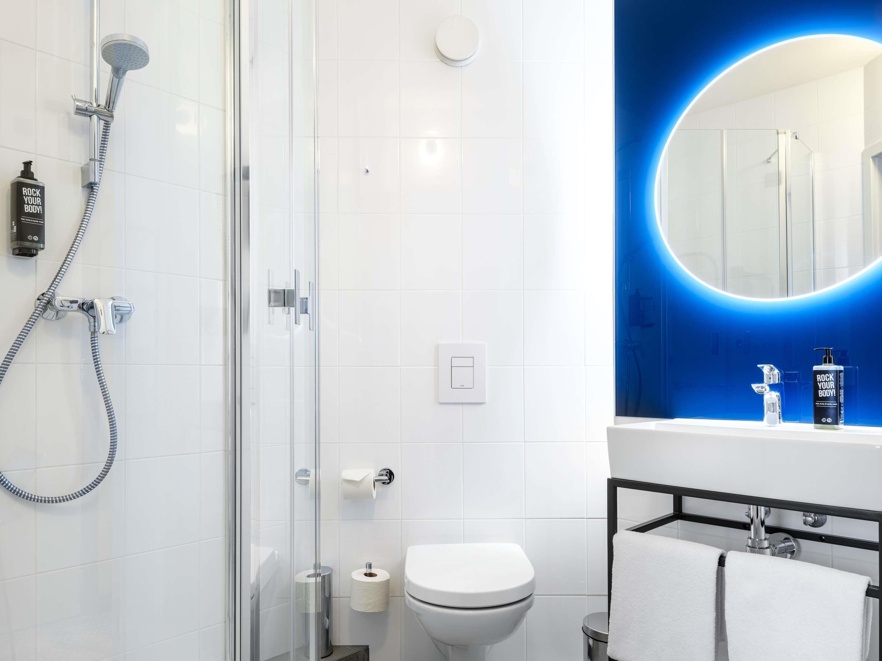Un baño moderno con cabina de ducha de vidrio, inodoro, lavabo con espejo y toallero.