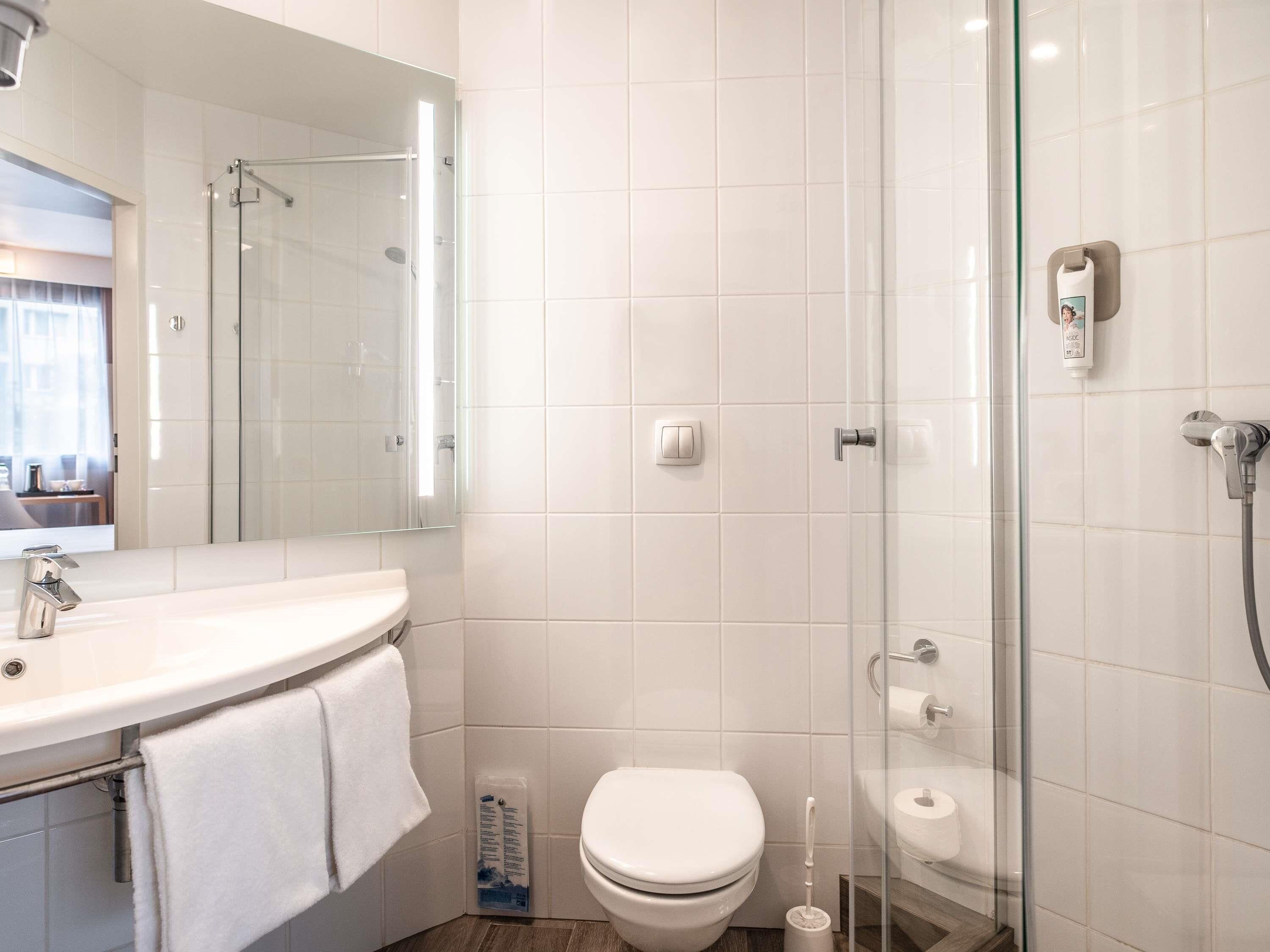 A modern bathroom with a glass shower enclosure, a white toilet, and a sink with a towel.