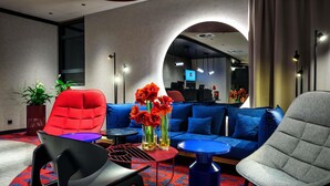 A modern hotel lobby with a blue sofa, red and grey chairs, a small table, and a potted plant. - ibis Krakow Centrum (Kraków)