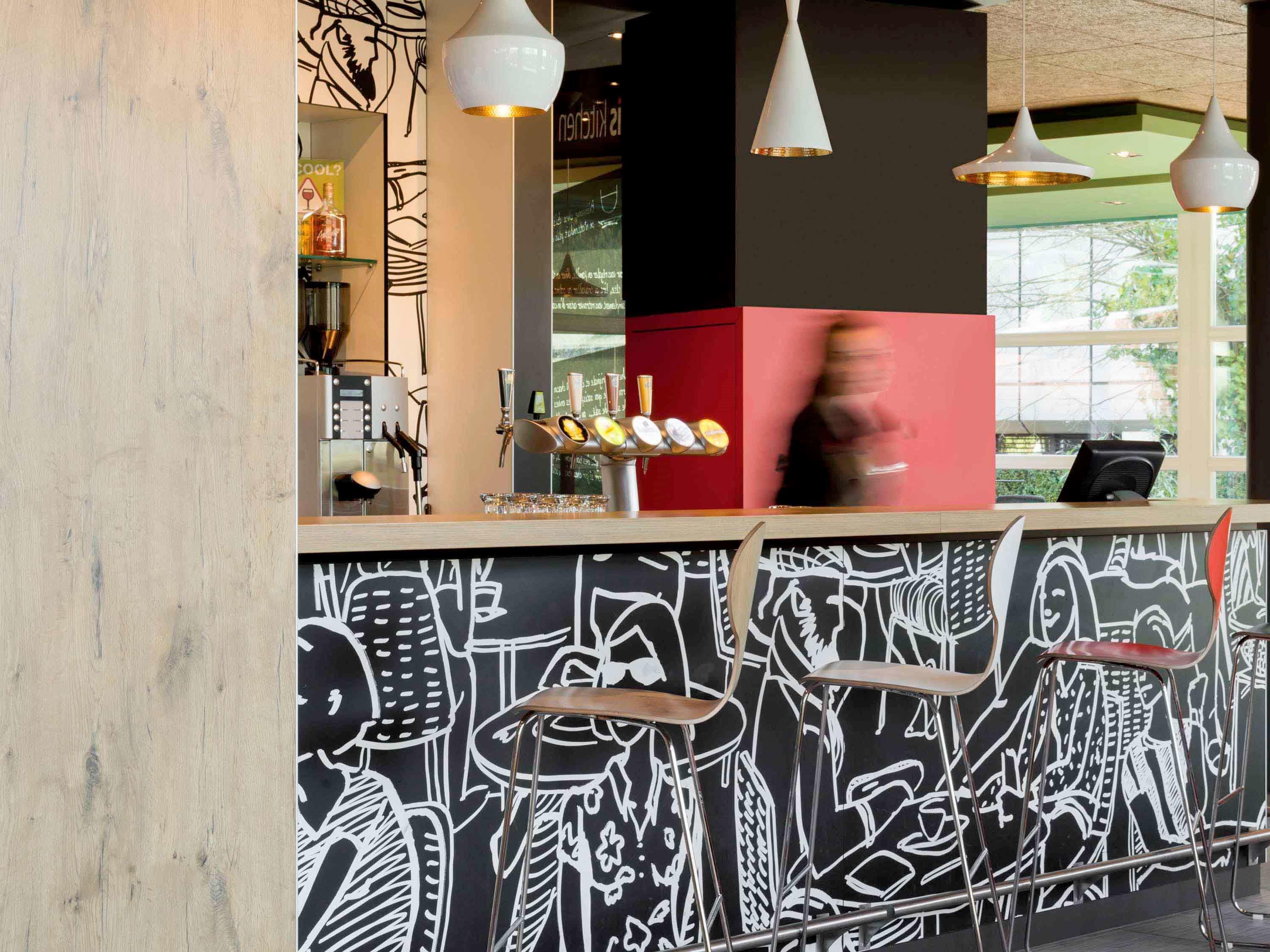 Eine Bar mit Wandgemälde in Schwarz und Weiß, moderner Pendelleuchten und einem roten Tresen.