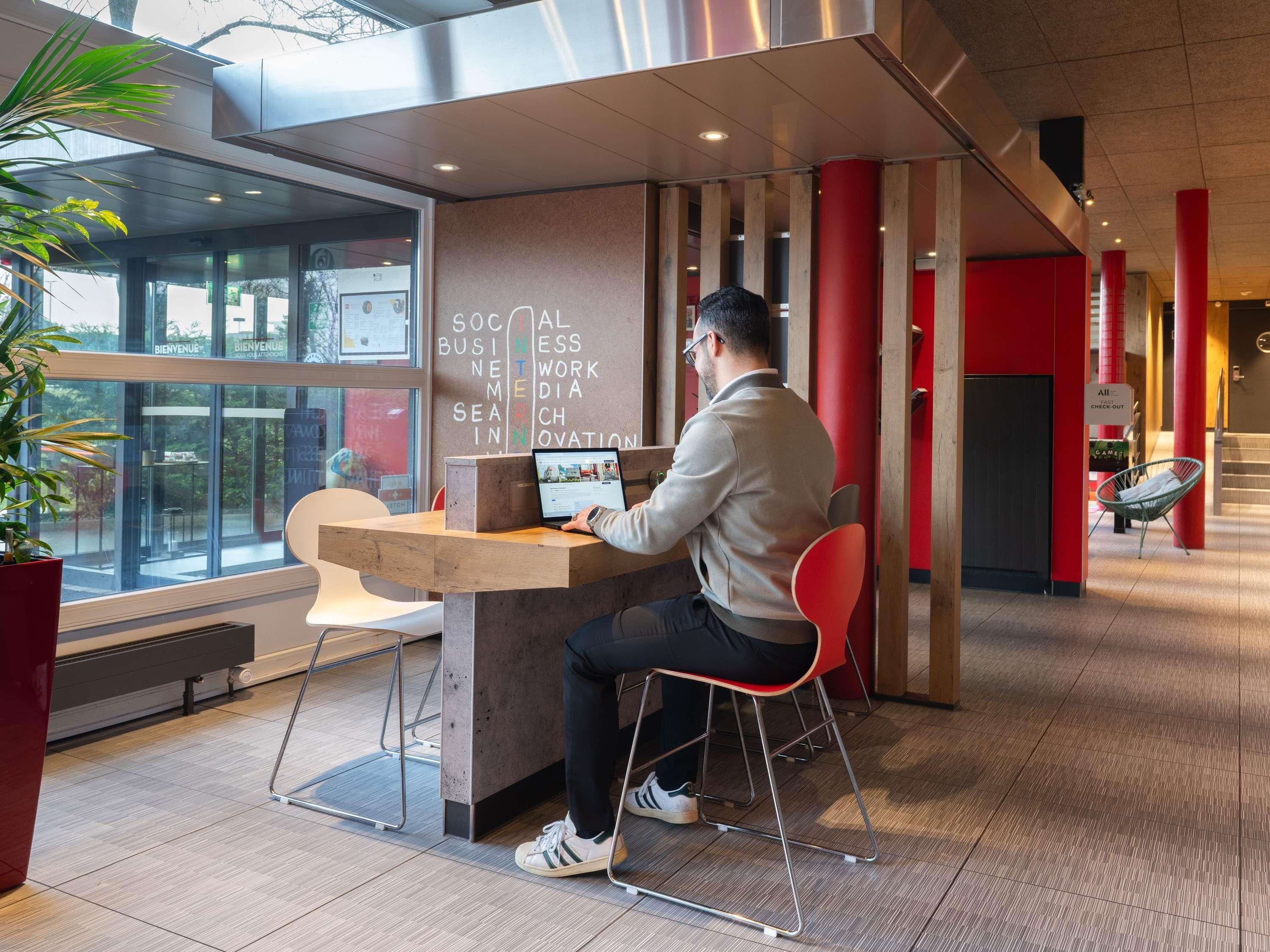 A man working at a desk with a laptop in a modern office space with large windows and red accents.