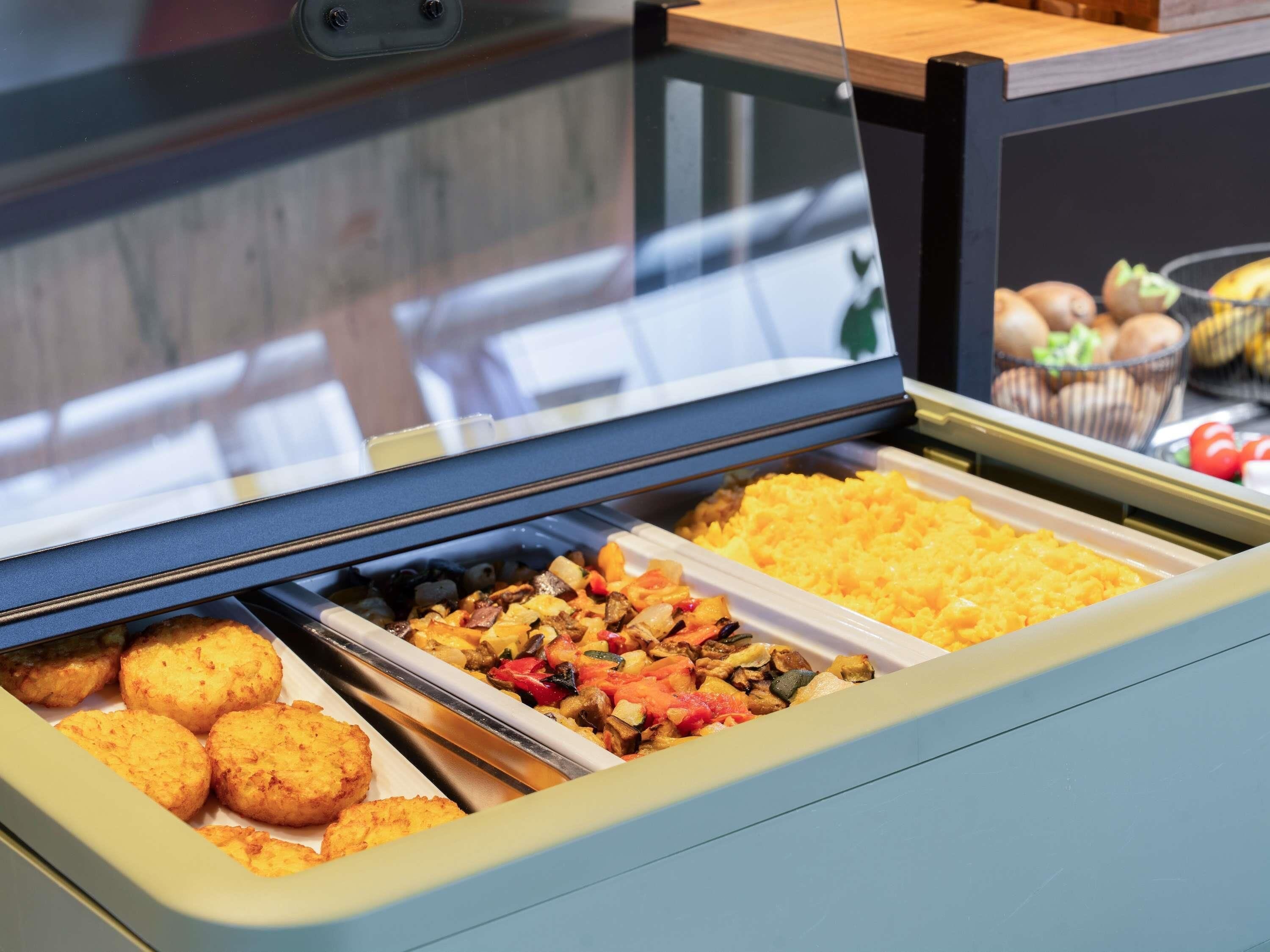 Buffet com diversos alimentos, incluindo ovos mexidos, legumes assados e frituras.
