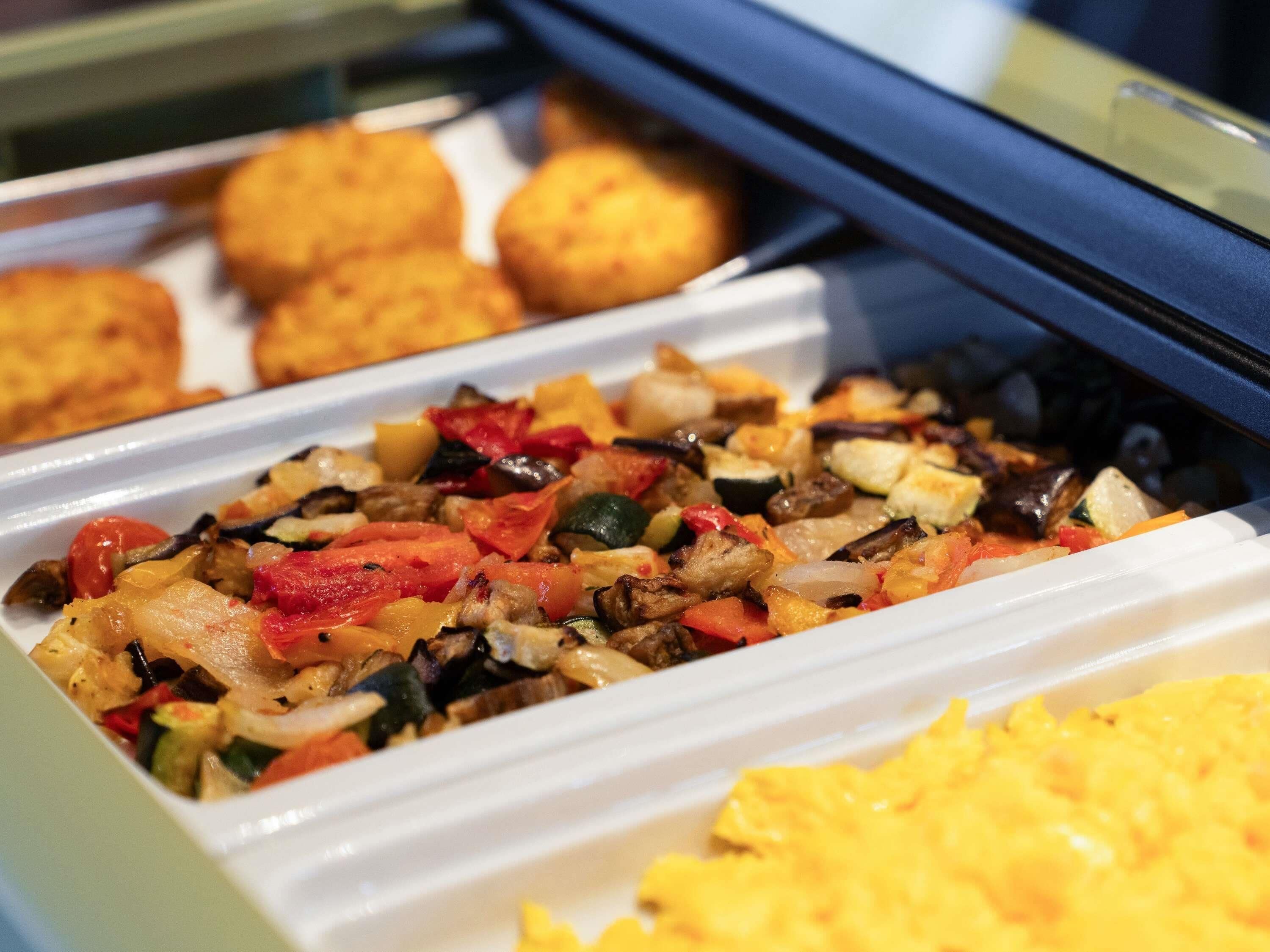 Un bufé con diversas opciones de comida, incluyendo un salteado de verduras, huevos revueltos y alimentos fritos.