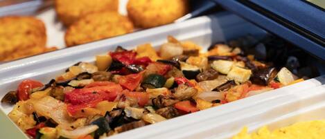Un bufé con diversas opciones de comida, incluyendo un salteado de verduras, huevos revueltos y alimentos fritos.