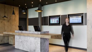 A reception area with a modern design, featuring a reception desk, pendant lighting, and digital displays on the wall. - ibis Geneve Aeroport (Meyrin)