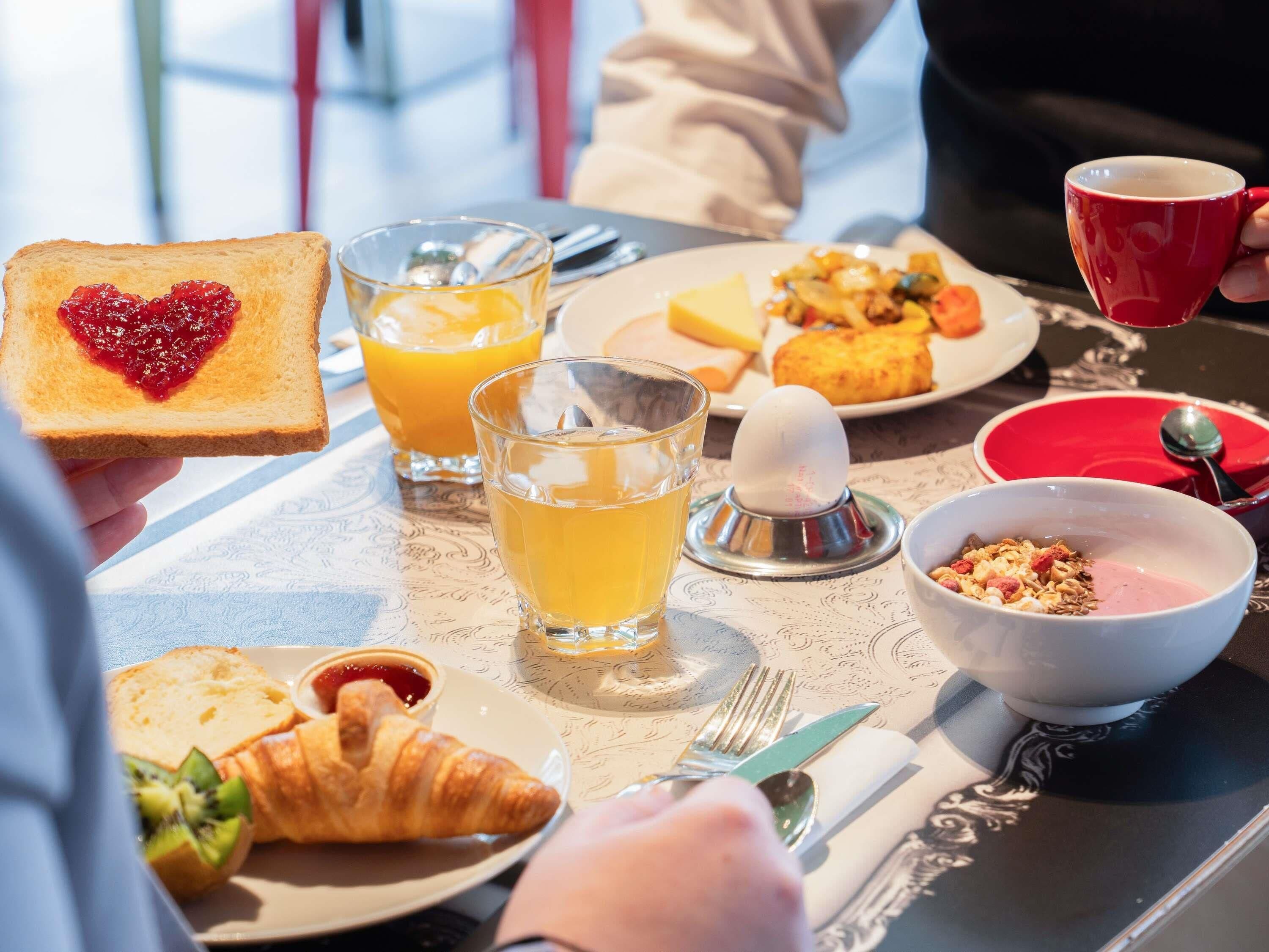 A breakfast setting with toast, juice, croissant, and a bowl of cereal.