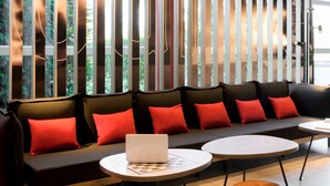 A modern seating area with a sofa and round tables, featuring a laptop on one of the tables. - ibis Geneve Aeroport (Meyrin)