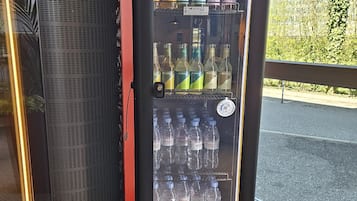 A beverage vending machine with multiple drink options, including water and various alcoholic beverages, located indoors near a window.