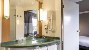 A hotel bathroom with a green sink, a mirror, a towel rack, and a shower area visible through the door.