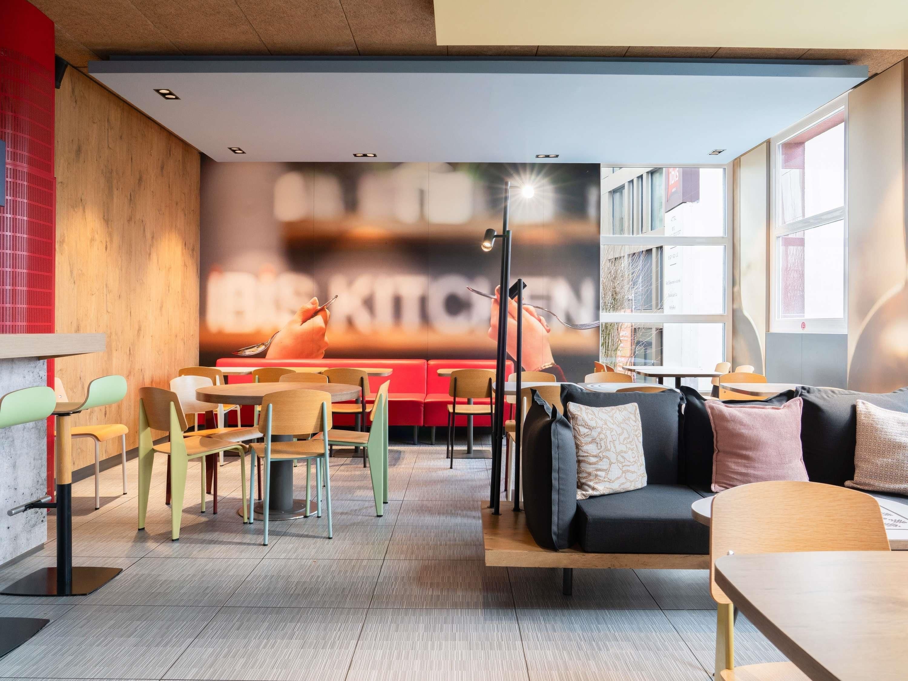 A modern cafe interior with seating arrangements, a large mural, and a view of the street.