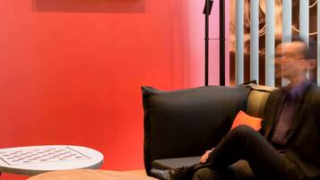 A modern interior with a red wall, a black sofa, and a round wooden table.