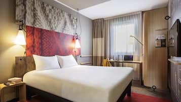 Habitación de hotel con una cama grande, un escritorio con una computadora portátil, un televisor y un mini bar.