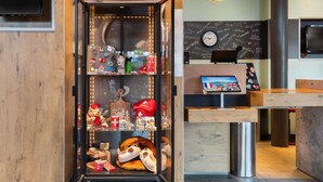 A reception area with a wooden desk, a digital welcome screen, and a wall with a clock and various stickers. - ibis Geneve Aeroport (Meyrin)