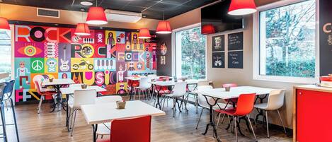 A vibrant restaurant interior with colorful wall art, red and white tables, and large windows.