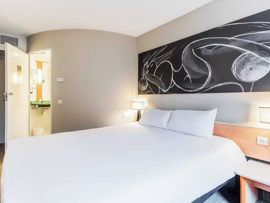 Habitación de hotel con una cama grande, una mesita de noche, un cuadro colgado en la pared y un baño visible a través de una puerta abierta.