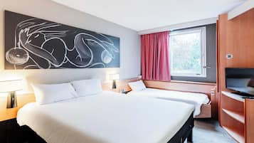 A hotel room with a large bed, two bedside tables with lamps, a TV, a window with red curtains, and a wall art piece.