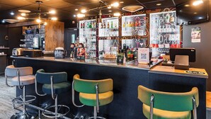 Zona de bar con mostrador, taburetes y estantes llenos de botellas y copas.