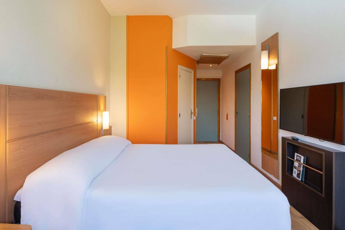 A hotel room with a large bed, a TV, and a door leading to another room.