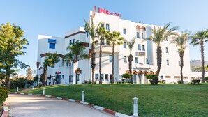 A modern hotel with a prominent "ibis HOTEL" sign, a restaurant, and a well-maintained lawn with palm trees. - ibis Meknes Hotel (Meknes)