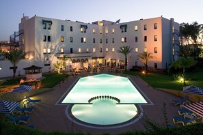 Relax by the central pool surrounded by lounge chairs and umbrellas, amidst lush lawns and palm trees.
