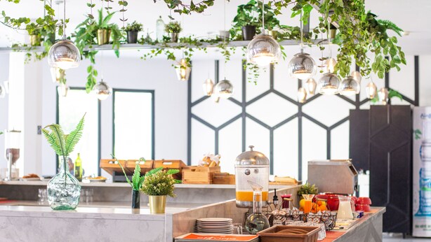A modern kitchen with hanging plants, pendant lights, and a breakfast bar with various items. - ibis Meknes Hotel (Meknes)