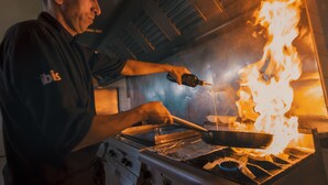 A chef cooking with a pan on a stove with flames. - ibis Meknes Hotel (Meknes)