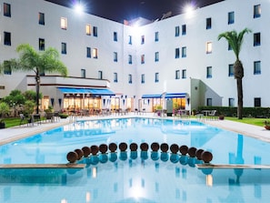 A hotel with a swimming pool, outdoor seating, and a building facade with multiple windows. - ibis Meknes Hotel (Meknes)