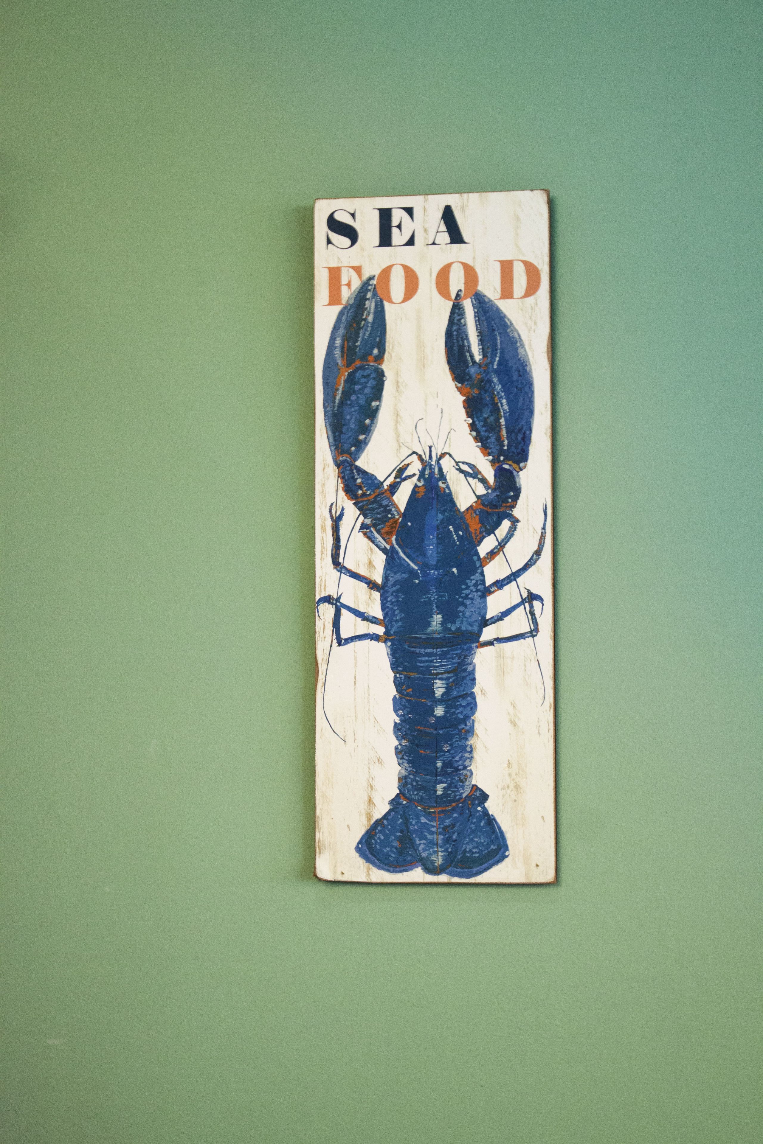 Une enseigne fixée au mur, représentant un homard et portant l'inscription « FRUITS DE MER ».