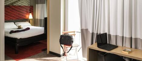 Habitación de hotel con cama, escritorio, silla y una pequeña mesa con objetos encima.