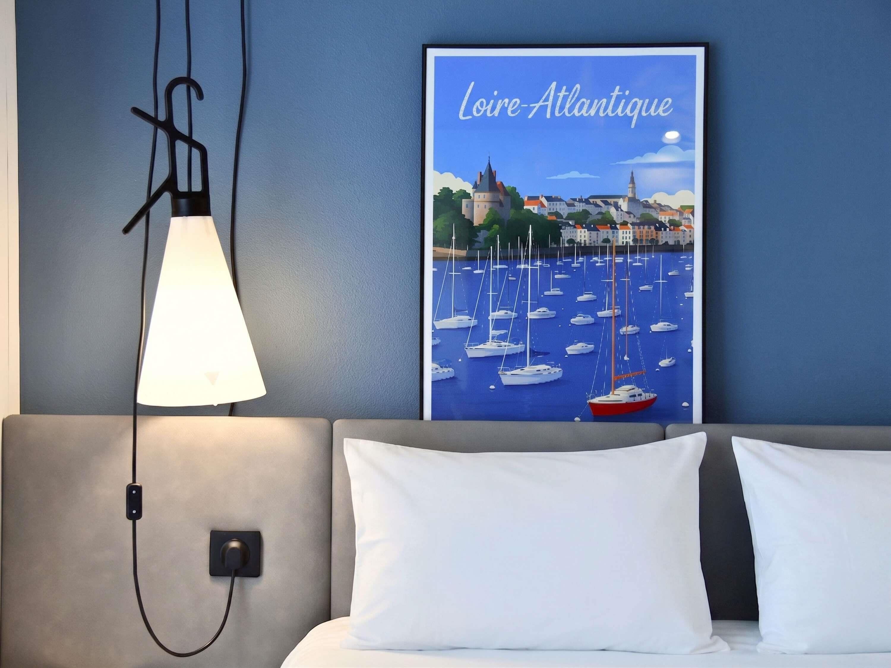 A hotel room with a bed, a wall-mounted lamp, and a poster of a harbor scene.